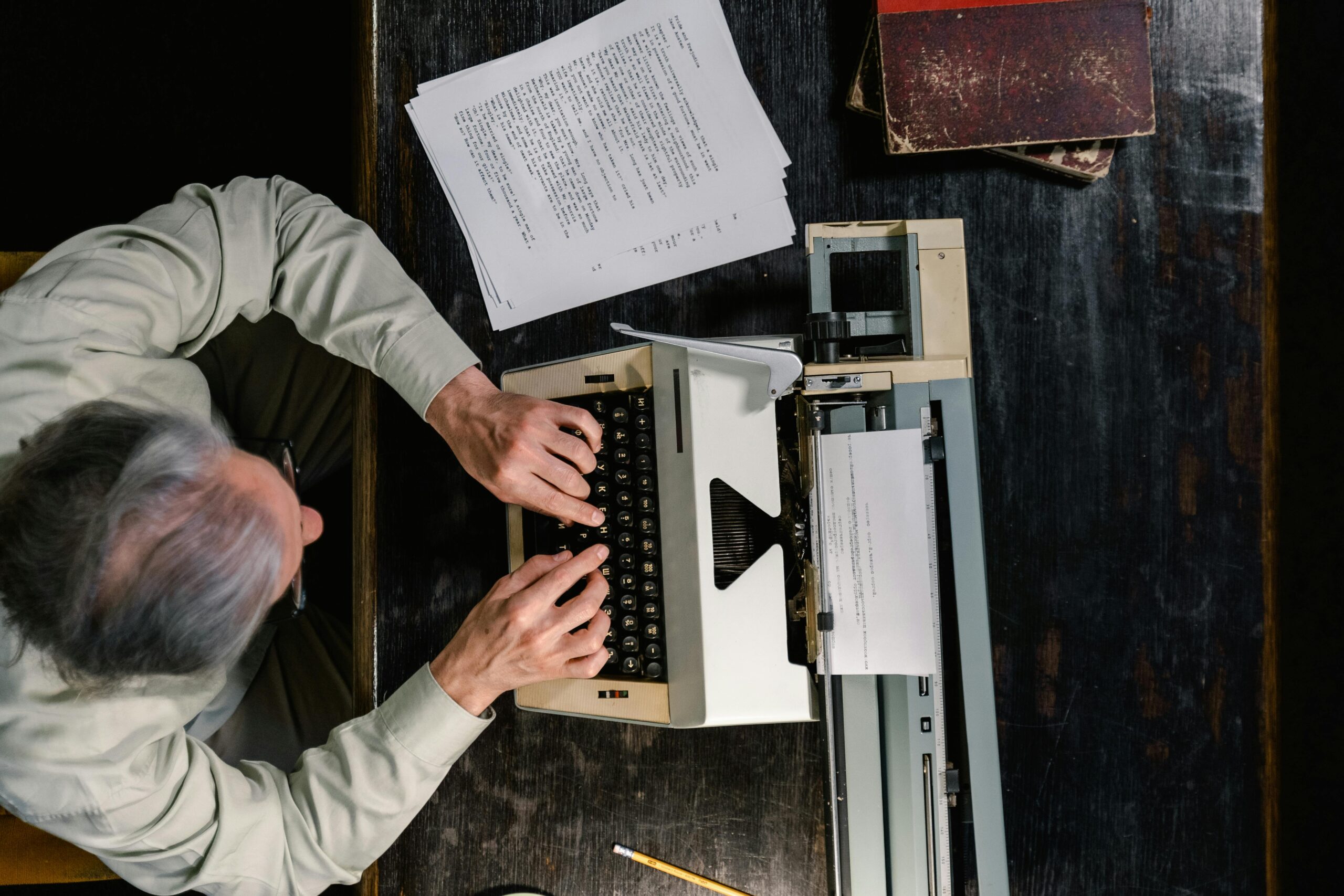 A person typing on a vintage typewriter with scattered papers on a wooden table.